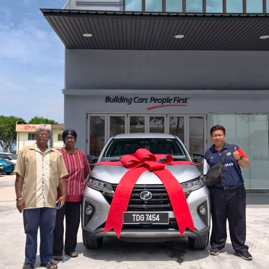 Pasangan pelanggan menerima Perodua Aruz baharu dengan riben merah di pusat jualan